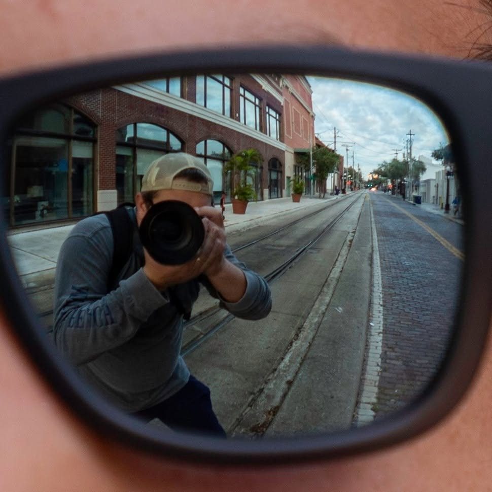 Self portrait of Stephen Stough reflected in sunglasses, shooting on a street in Ybor City